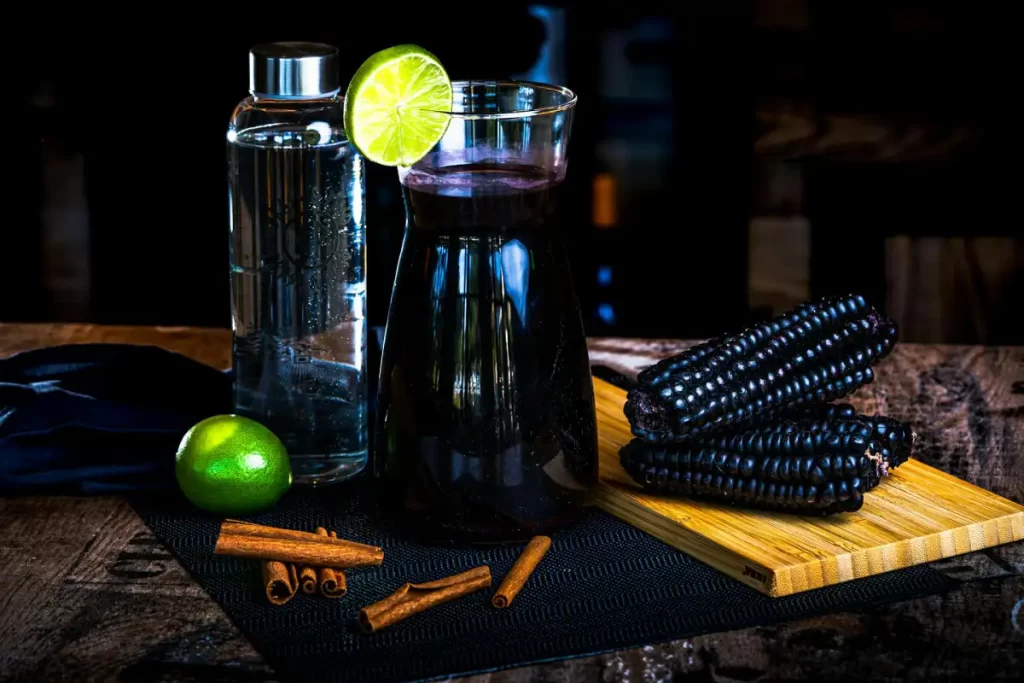 Peruvian Cuisine Guide: The Most Iconic Dishes and Drinks You Must Try 9 A jar of Chicha Morada surrounded by purple corn, cinnamon sticks, and fresh lemons, showcasing the natural ingredients of this traditional Peruvian beverage.