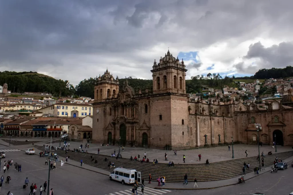 Panoramic view of the Cusco Cathedral and Plaza de Armas with colonial buildings and Andes mountains in the background.