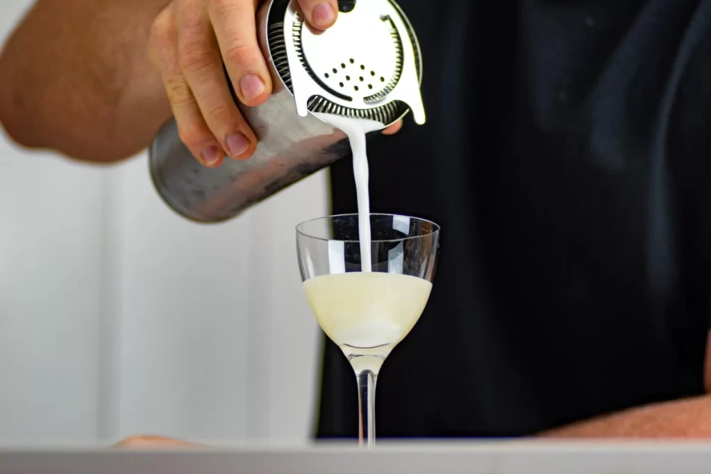 Peruvian Cuisine Guide: The Most Iconic Dishes and Drinks You Must Try 8 A bartender pouring a freshly made Pisco Sour, Peru’s national cocktail, into a glass topped with a light foam and a dash of Angostura bitters.